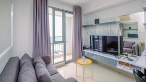A modern living room with a grey sofa, a flat-screen TV, a small round table with a bottle, and a balcony with purple curtains.