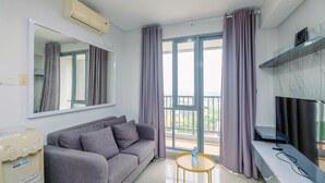 A modern living room with a grey sofa, a large mirror, a flat-screen TV, and a balcony with purple curtains.