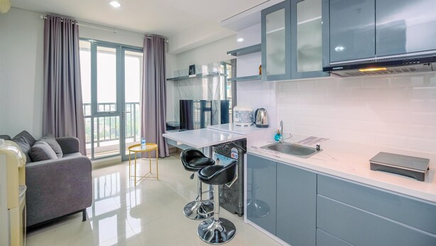 A modern kitchen with grey cabinets, a white countertop, and a built-in oven. There is a bar stool near the sink and a grey sofa in the living area.