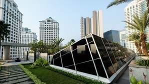 A modern building with a unique geometric design, surrounded by well-maintained greenery and tall residential buildings in the background. - Stunning And Comfy Studio Apartment At Citylofts Sudirman (Jakarta)