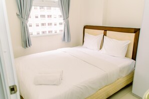 A neatly made bed with white linens and pillows, a wooden headboard, and a window with curtains.