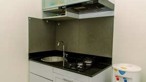A compact kitchen with a sink, stove, and a trash bin. - Modern Look 2Br Green Pramuka City Apartment Near Mall (Jakarta)