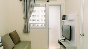 A small, modern room with a sofa, a television, and a window with curtains. - Modern Look 2Br Green Pramuka City Apartment Near Mall (Jakarta)