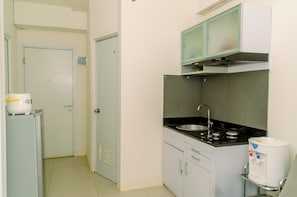 A compact kitchen with a stove, sink, and a microwave above the counter. There is a refrigerator to the left and a water dispenser to the right.