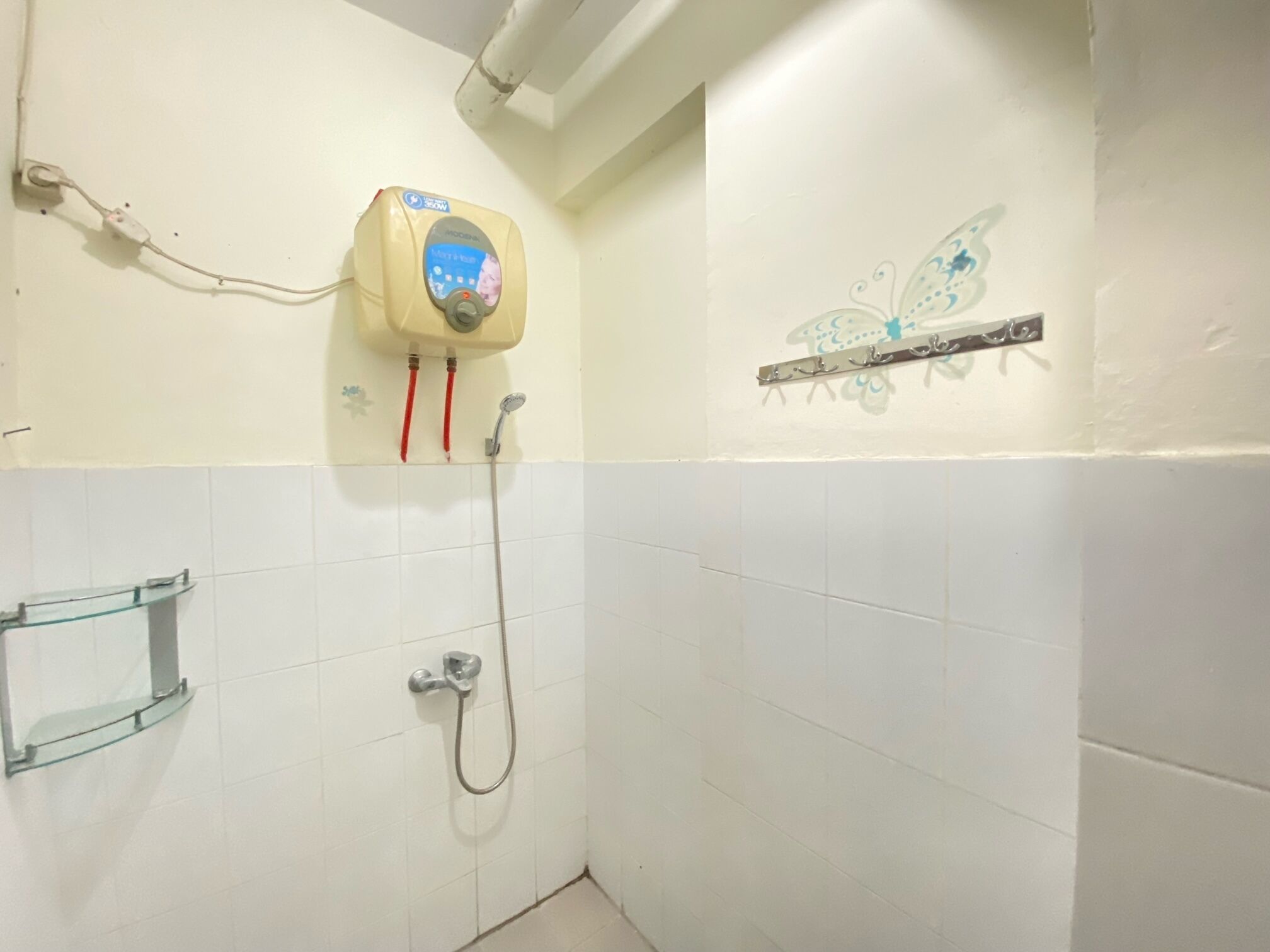 A bathroom with white tiled walls, a shower with a handheld showerhead, and a wall-mounted water heater with a digital display.