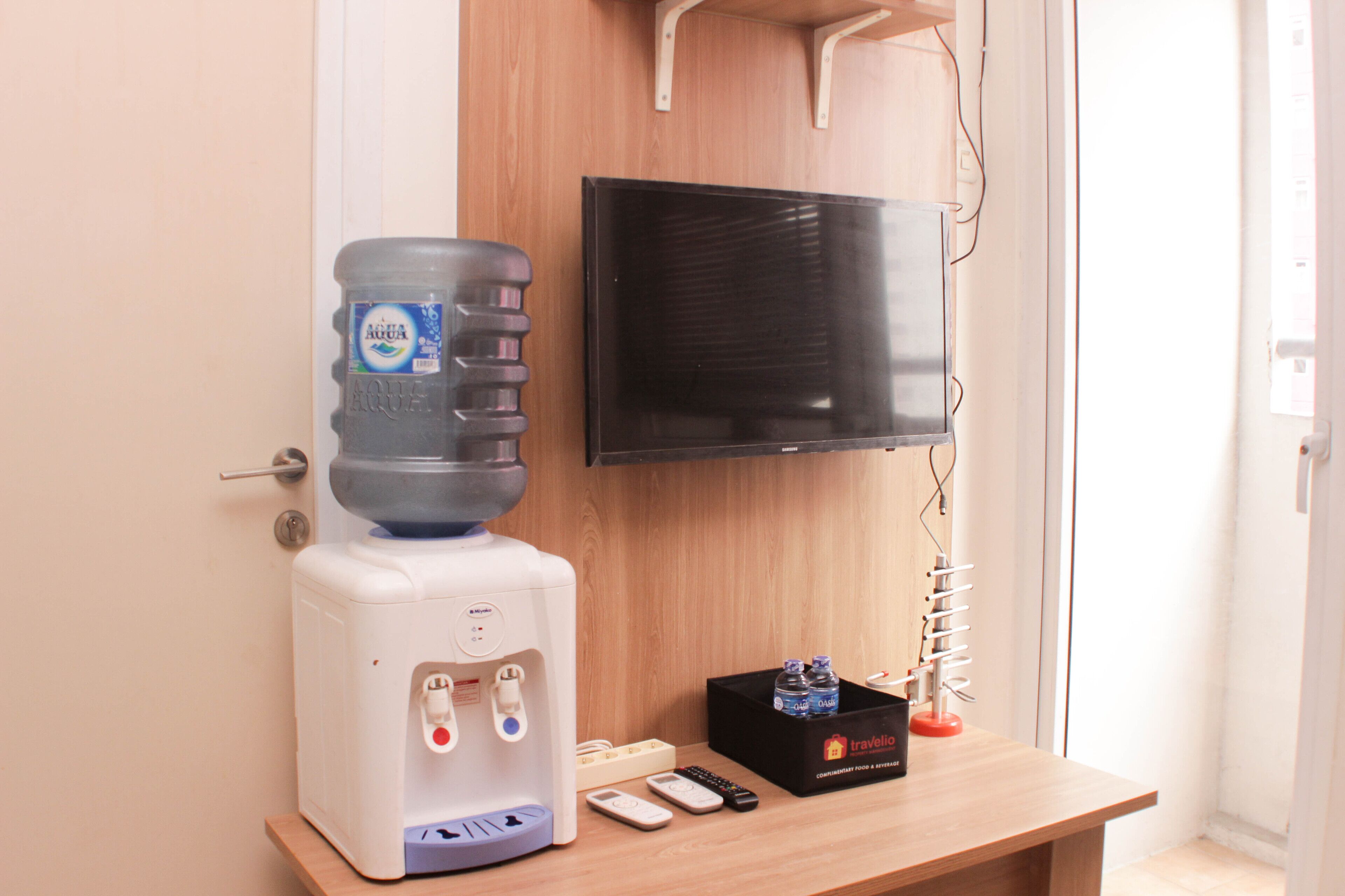Un dispensador de agua, un control remoto, un teléfono inteligente, una caja negra y un televisor montado en la pared.
