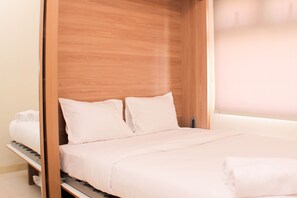 A neatly made bed with white linens and pillows, a wooden headboard, and a small shelf with towels.