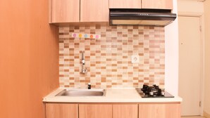A kitchen with a tiled backsplash, a stainless steel sink, wooden cabinets, and a black range hood. - Comfort 2Br At Green Pramuka Apartment (Jakarta)