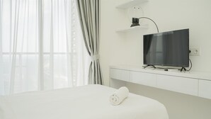 Una habitación de hotel con una cama, un televisor montado en la pared y una ventana con cortinas.