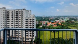 A high-rise building with multiple floors and balconies, overlooking a residential area with houses and greenery. - Fancy And Nice Studio Room At Casa De Parco Apartment (Pagedangan)
