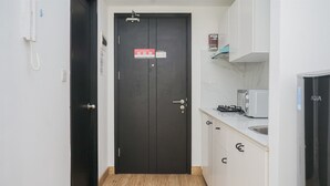 A narrow hallway with a black door, white cabinets, a microwave, and a refrigerator. - Fancy And Nice Studio Room At Casa De Parco Apartment (Pagedangan)