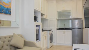 Een kleine keuken met witte kasten, een ingebouwde magnetron, een wasmachine en een roestvrijstalen koelkast.