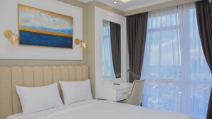 Een hotelkamer met een groot bed, een bureau, een stoel, een schilderij en een raam met gordijnen.