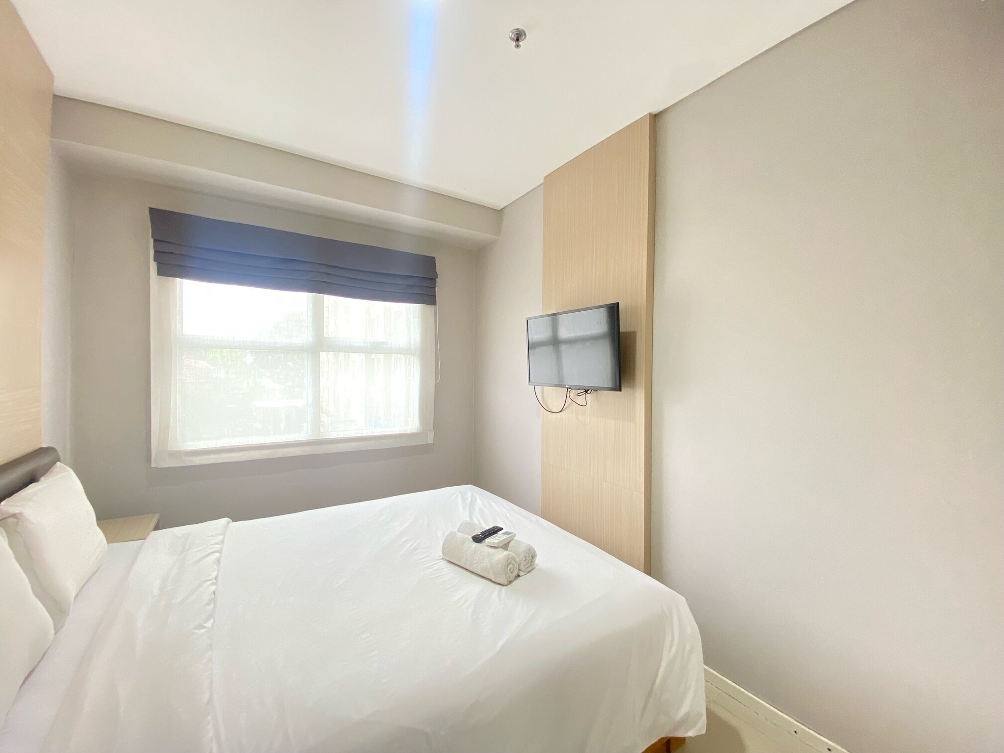 Ein Hotelzimmer mit einem Bett, einem an der Wand befestigten Fernseher und einem Fenster mit Vorhängen.