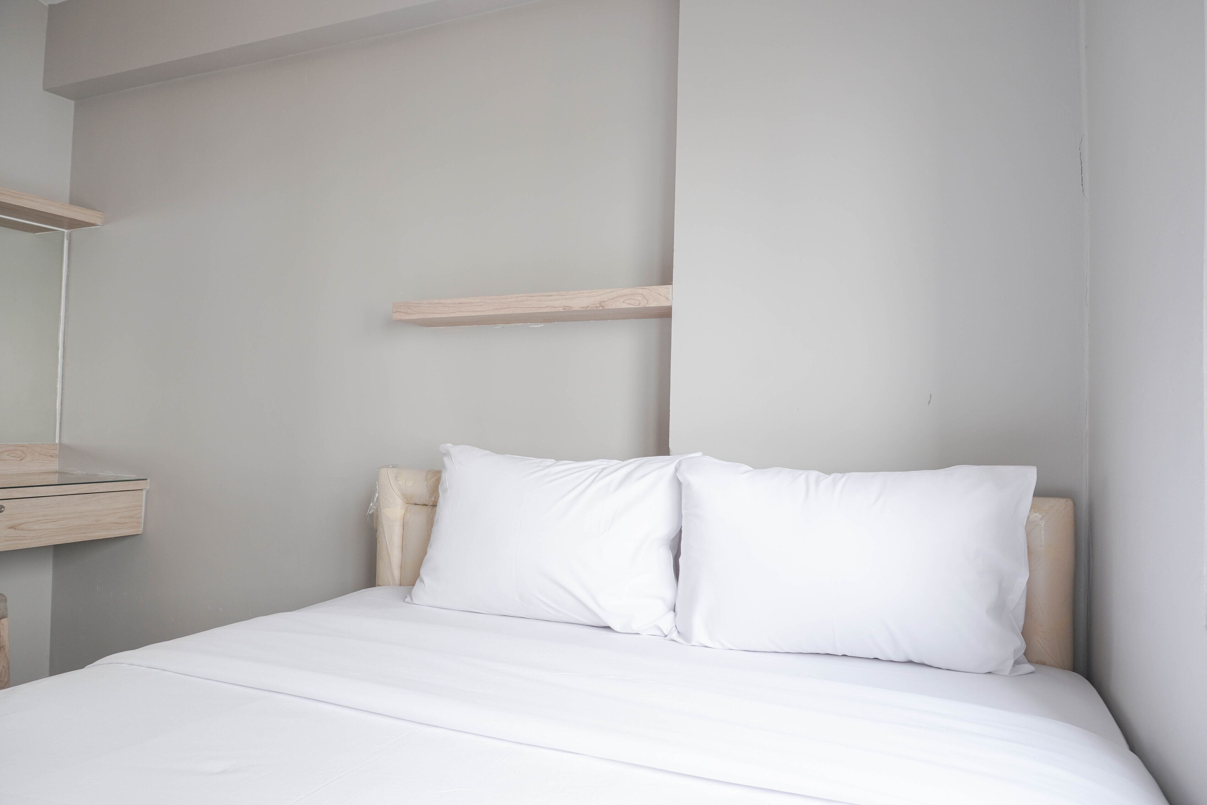 A minimalist bedroom with a bed, white bedding, and a wooden headboard.