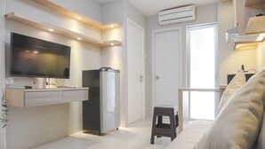 A compact living space with a flat-screen TV mounted on a wall, a built-in refrigerator, a small stool, and a sofa.