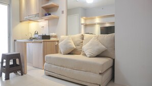 A modern living space with a sofa, a small stool, and a kitchenette area.