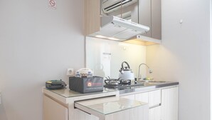 A compact kitchen with a gas stove, a kettle, a sink, and a travel bag on the counter. - Well Designed And Cozy Studio At Bassura City Apartment (Jakarta)