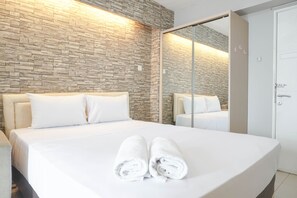 Una habitación de hotel moderna con una pared de piedra, una cama grande con ropa de cama blanca y un armario espejado.