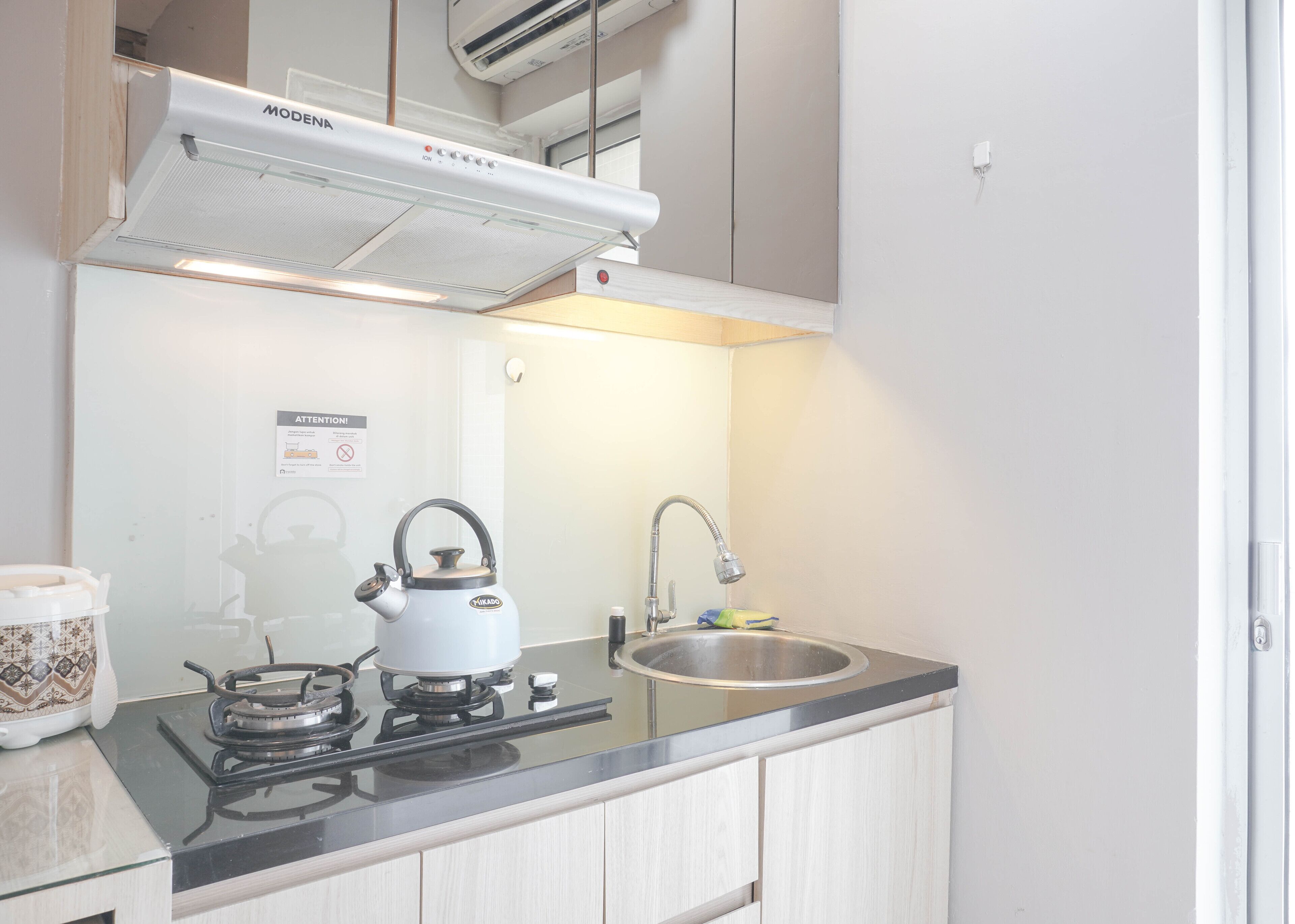 Une cuisine compacte équipée d’une cuisinière à gaz, d’une bouilloire, d’un évier et d’une hotte d’extraction fixée au plafond.