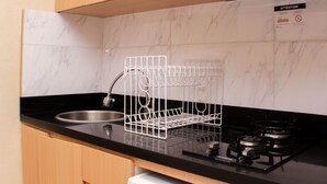 Una cocina con encimera negra, pileta de acero inoxidable, escurridor blanco y estufa a gas.
