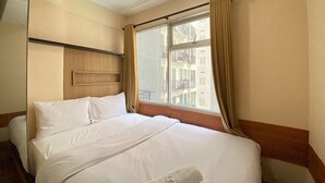Habitación de hotel con cama, ventana con cortinas, cabecera de madera y vistas a edificios.