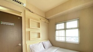 Ein Einzelbett mit weißer Bettwäsche, ein Holz-Kopfteil, ein Fenster mit Jalousien und eine Tür mit Handtuchhalter.