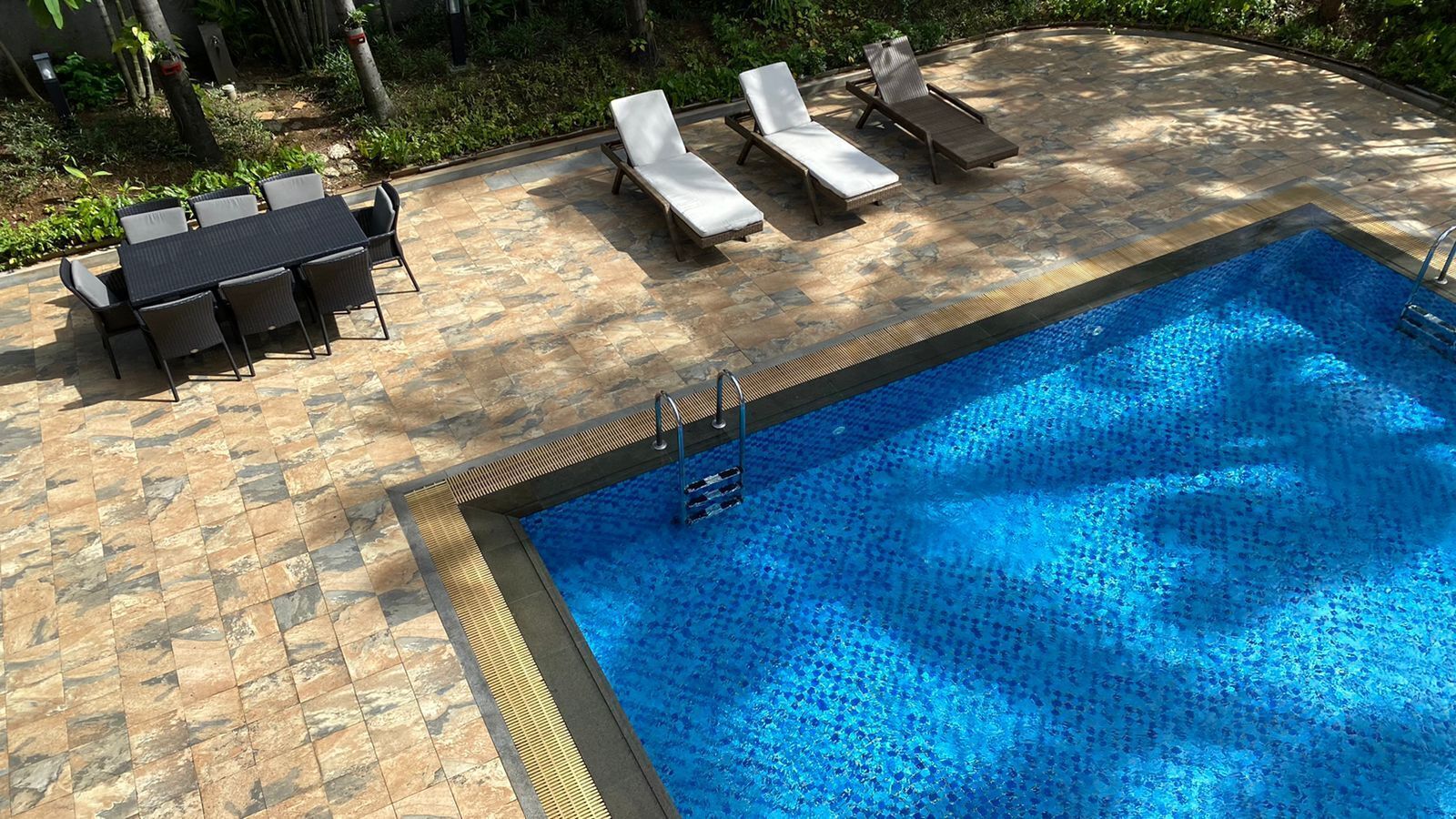 A swimming pool with lounge chairs and a table, surrounded by stone tiles.
