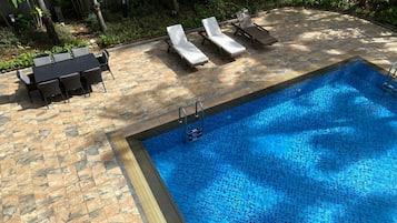 A swimming pool with lounge chairs and a table, surrounded by stone tiles.