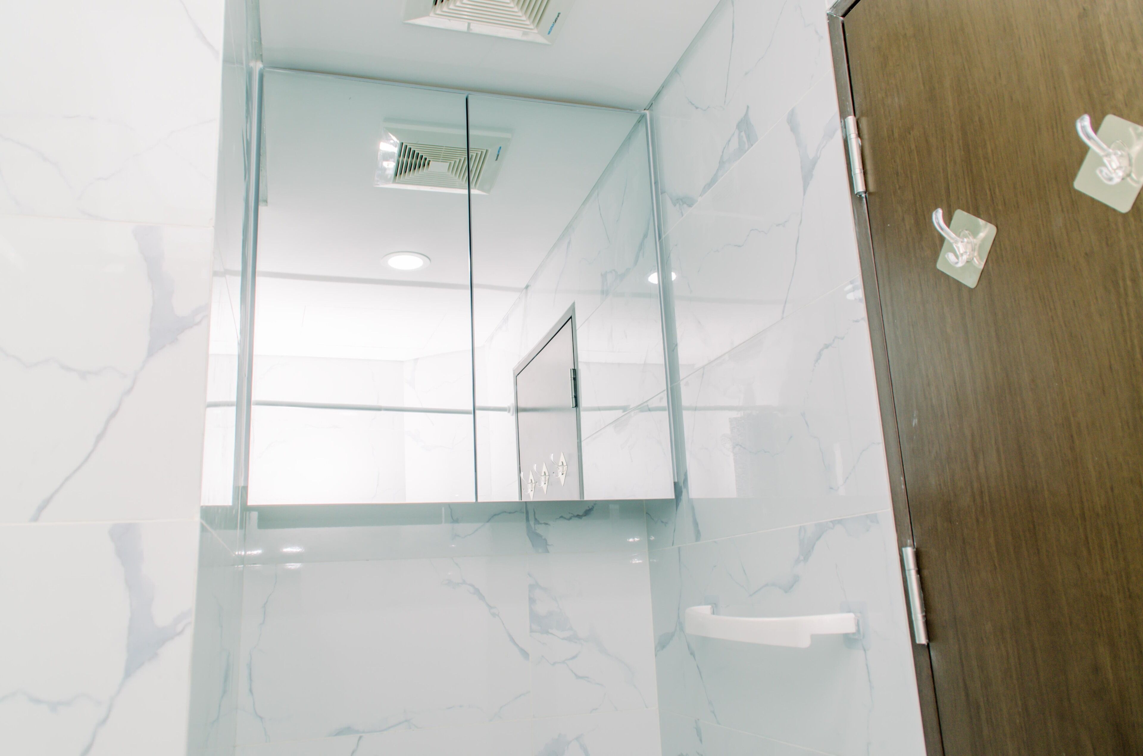 A modern bathroom with a glass shower enclosure, marble walls, and a wooden door.