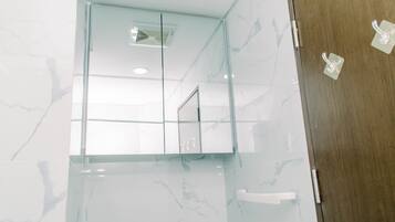 A modern bathroom with a glass shower enclosure, marble walls, and a wooden door.