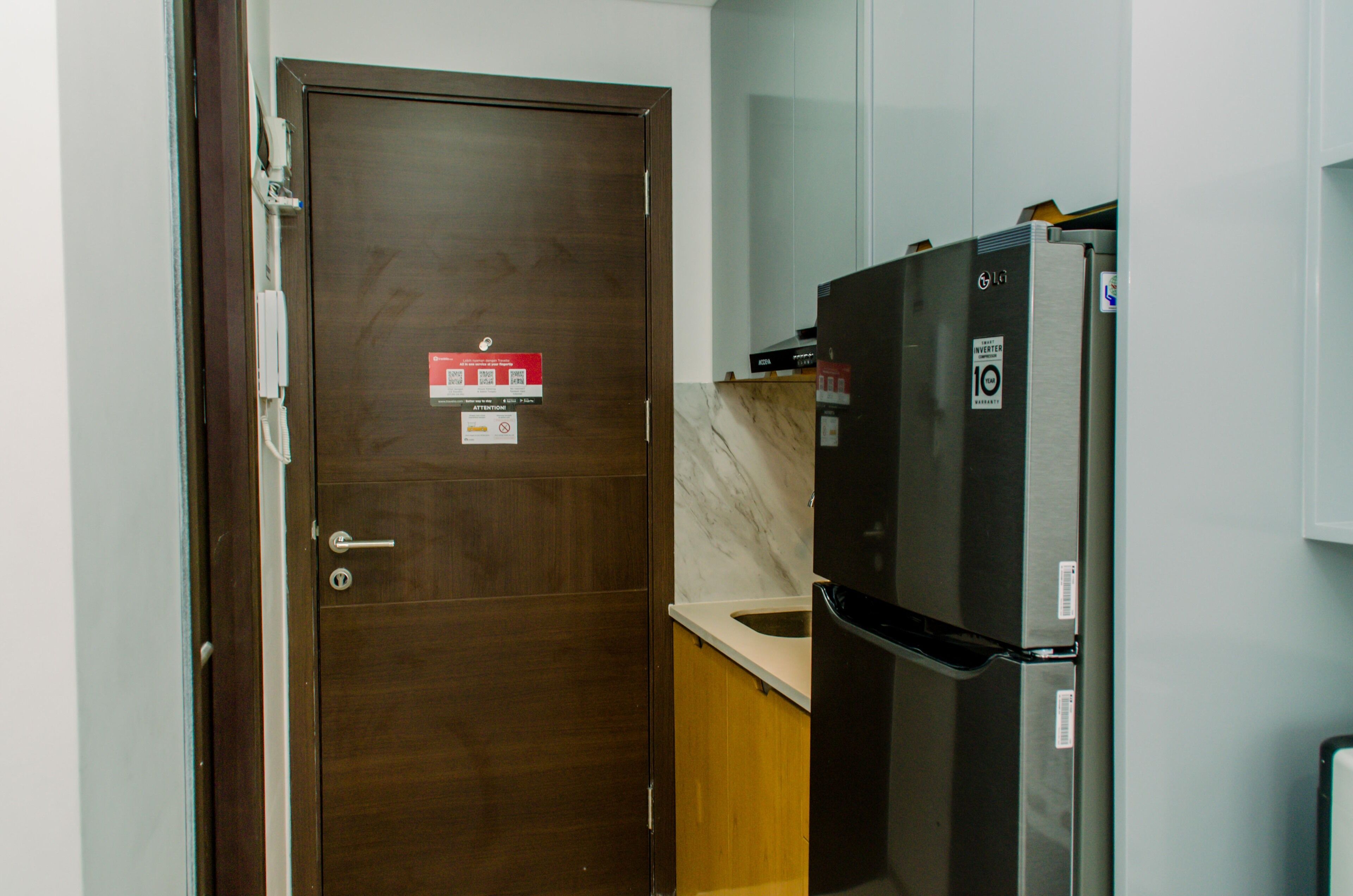 A compact kitchen with a wooden door, a stainless steel refrigerator, and a marble countertop.