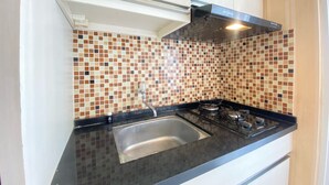 A kitchen with a black countertop, a stainless steel sink, and a tiled backsplash. - Classic Private 1Br Apartment At Parahyangan Residence Bandung (Bandung)