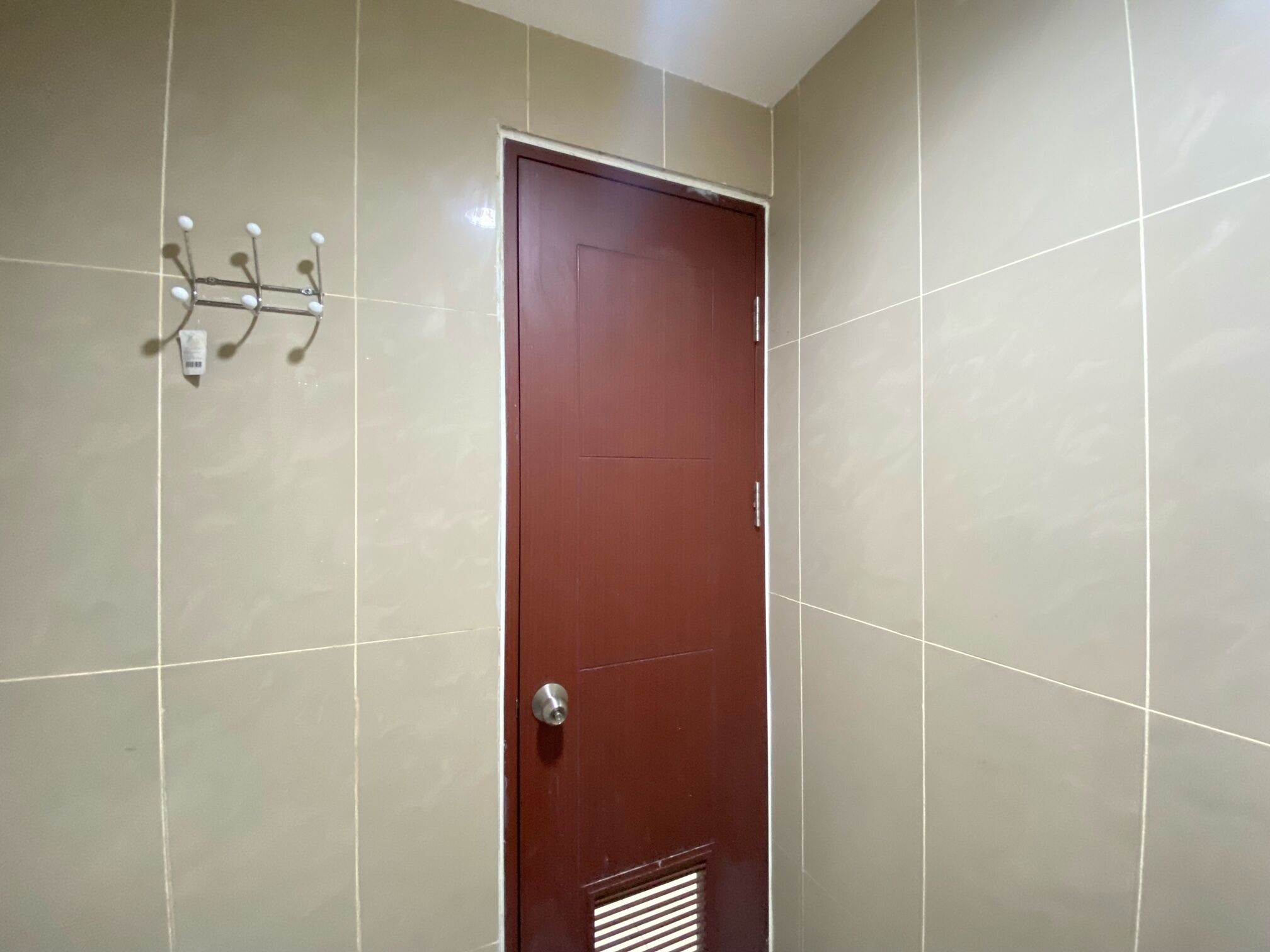 A room with a wooden door, beige tiled walls, and a wall-mounted towel rack.