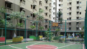 An outdoor basketball court surrounded by a green fence, with a playground in the background and a multi-story building with balconies. - Spacious 2Br At Gateway Ahmad Yani Apartment (Bandung)