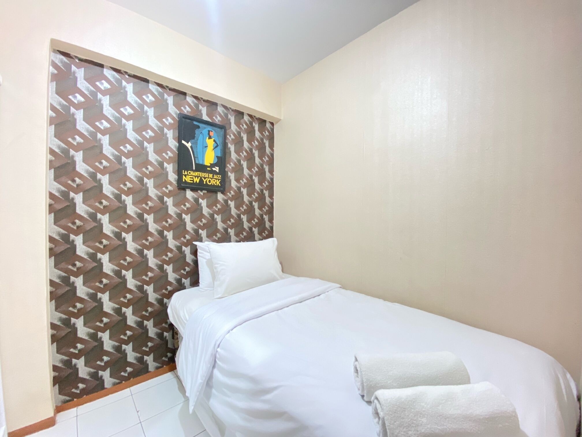 A single bed with white bedding and pillows, a patterned wall, and a poster of a jazz musician.