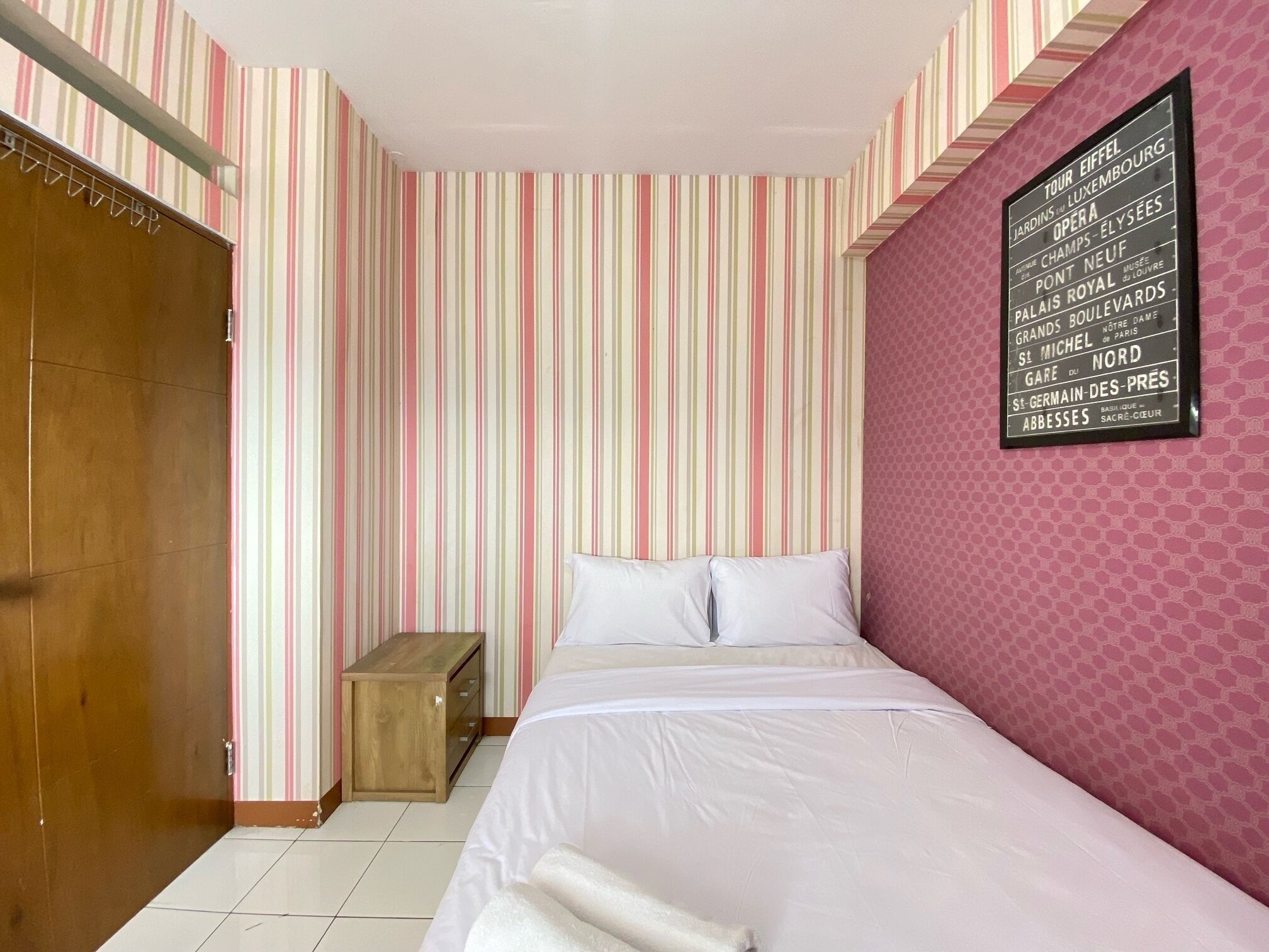 A hotel room with a striped wallpaper, a bed with white linens, a wooden bench, and a wall-mounted sign listing hotel amenities.