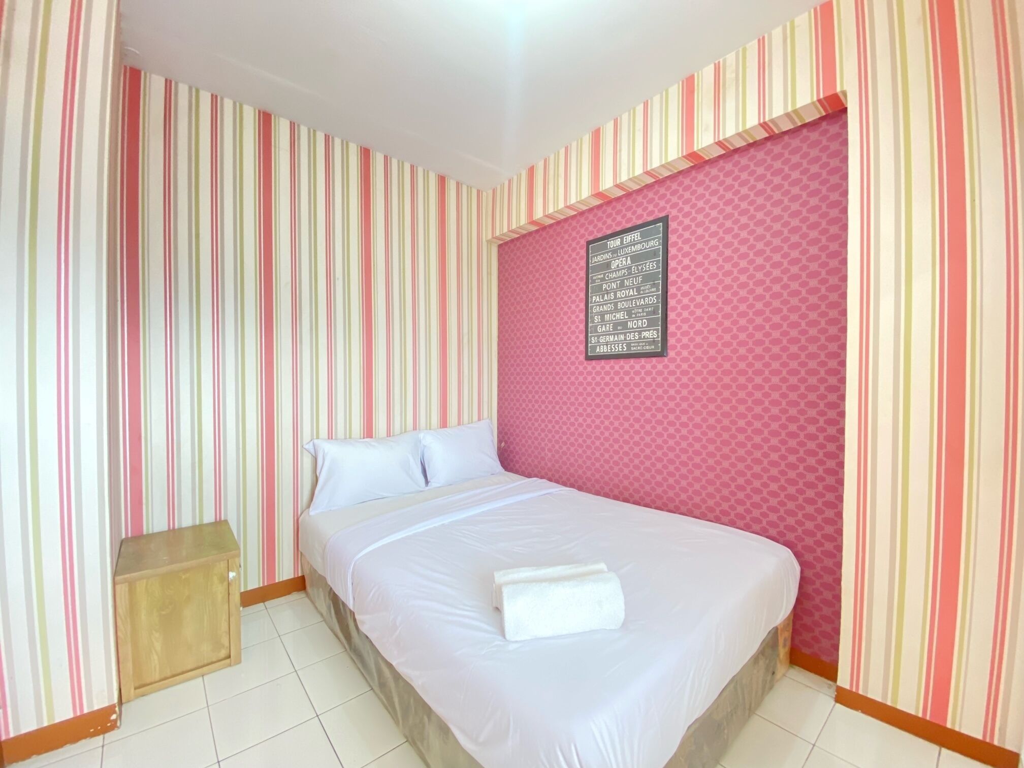 Una camera d'hotel con un letto, un comodino in legno e una parete con un cartello che elenca le attrazioni nei dintorni.