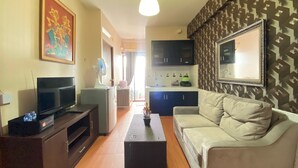 A living room with a sofa, a TV, a coffee table, and a kitchen area in the background. - Spacious 2Br At Gateway Ahmad Yani Apartment (Bandung)