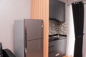 A compact kitchen with a refrigerator, a tiled backsplash, and a black curtain.