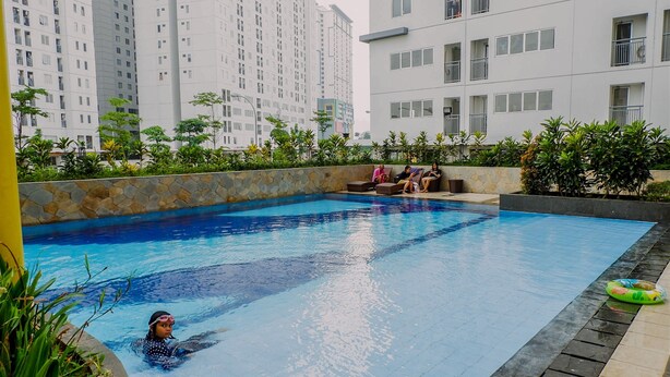 A swimming pool with a stone wall and plants, surrounded by high-rise buildings. - Comfort And Restful 2Br At Bassura City Apartment (Jakarta)