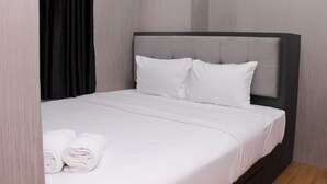 A neatly made bed with white linens and pillows, a dark headboard, and a wooden floor. - Comfort And Restful 2Br At Bassura City Apartment (Jakarta)