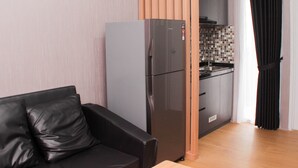 A compact living space with a kitchenette, a black leather sofa, and a refrigerator. - Comfort And Restful 2Br At Bassura City Apartment (Jakarta)
