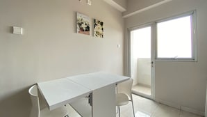 A minimalist room with a white table and chairs, two wall-mounted artworks, and a large sliding glass door leading to an outdoor area. - Cozy 2Br Apartment At Newton Residence Bandung (Bandung)