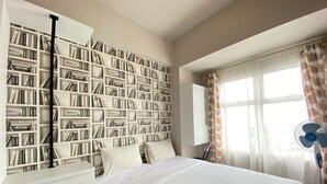 A bedroom with a large bookshelf, a bed, a desk, and a window with curtains. - Cozy 2Br Apartment At Newton Residence Bandung (Bandung)