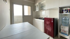 A compact kitchen with white cabinets, a red refrigerator, a water dispenser, and a window providing natural light. - Cozy 2Br Apartment At Newton Residence Bandung (Bandung)