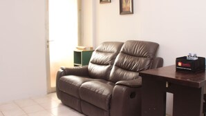 A living room with a brown leather sofa, a wooden coffee table, and a door leading to another room.