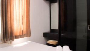A hotel room with a bed, a small bedside table, a mirror, and a window with curtains.
