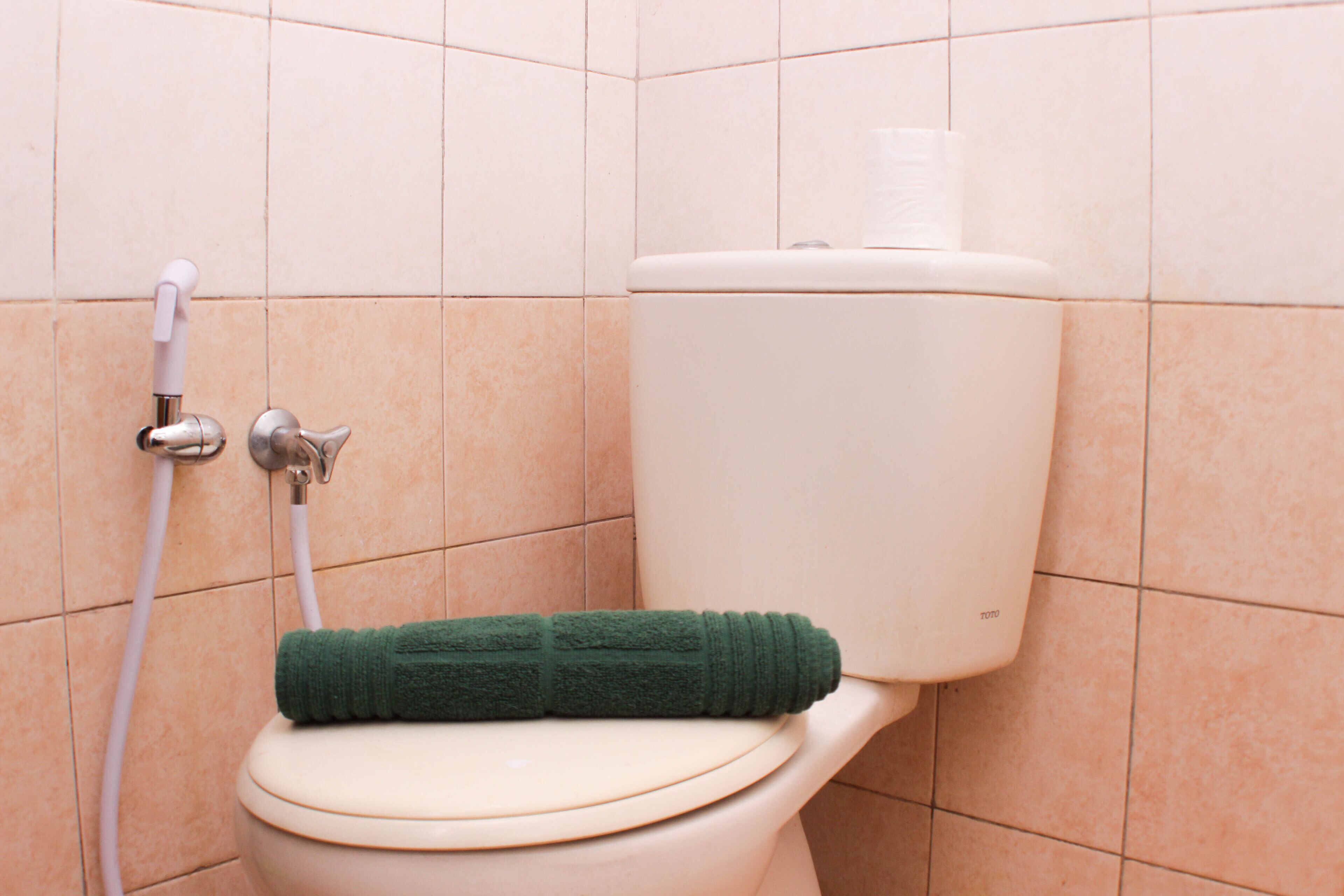 A toilet with a green towel on the seat and a toilet paper holder on the wall.