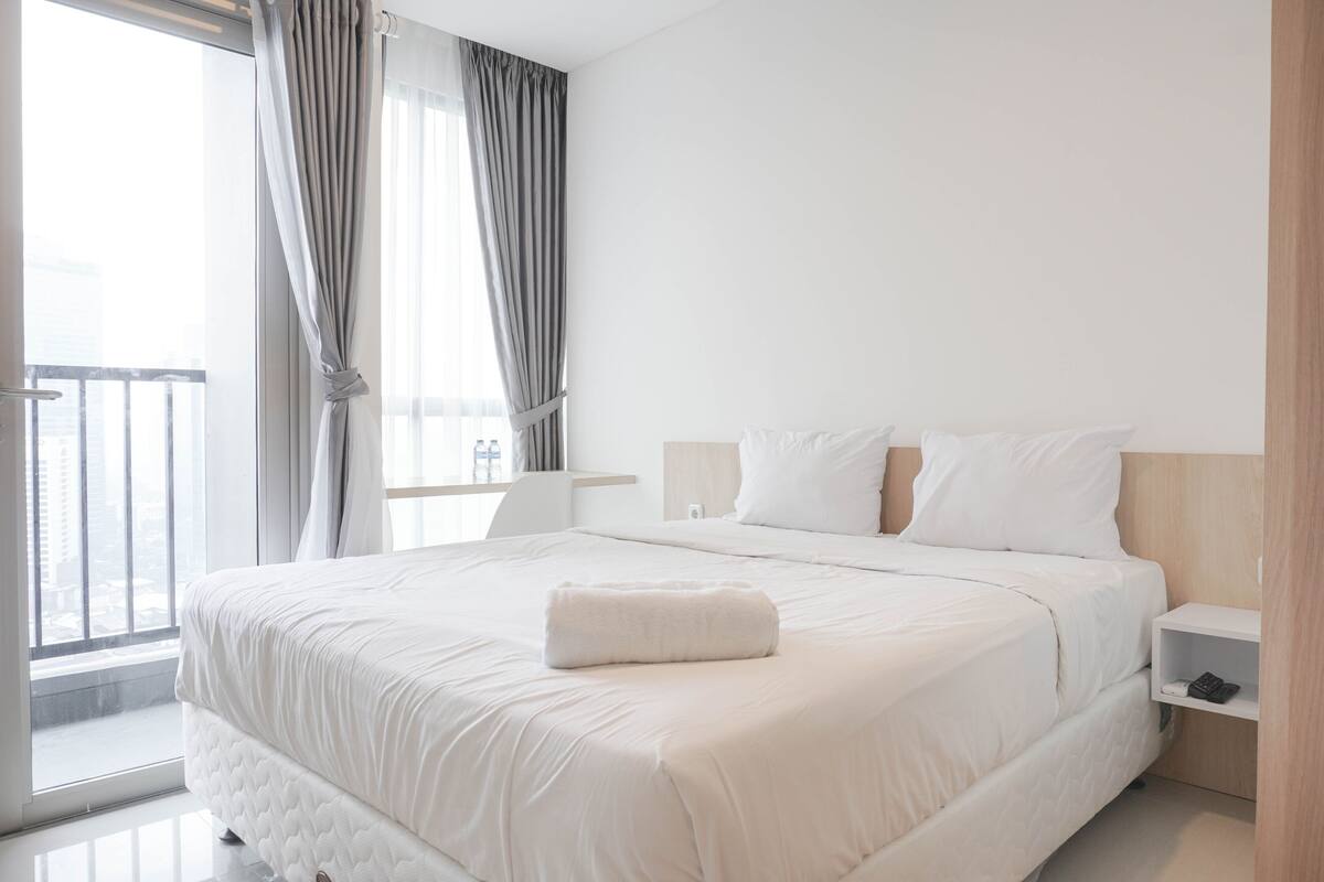 A modern hotel room with a large bed, a bedside table, a nightstand, and a view of the city through the window.